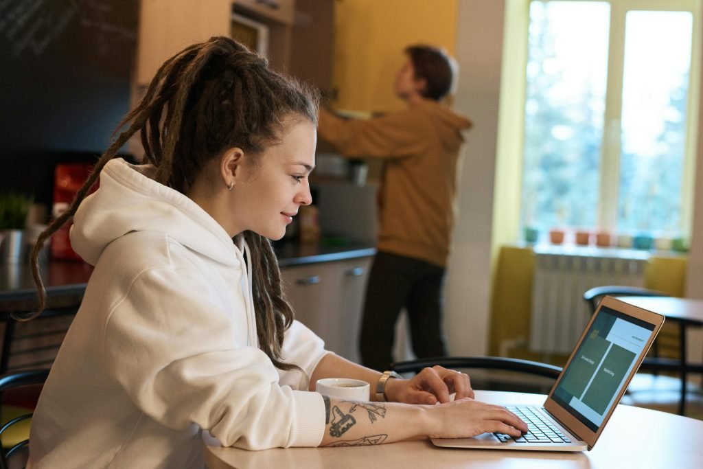 pexels-photo-3182792-3182792 Young woman with dreadlocks works on a laptop in a casual kitchen environment.