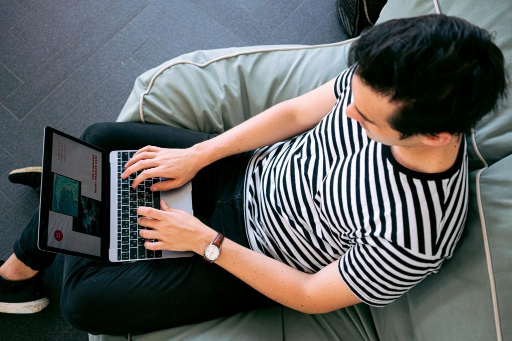 pexels-photo-3194523-3194523 A man in a striped shirt using a laptop on a bean bag, embodying relaxed productivity.