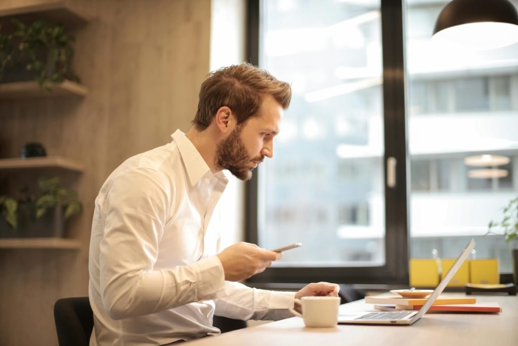 pexels-photo-926390-926390 Focused businessman working on laptop while checking smartphone in modern office.